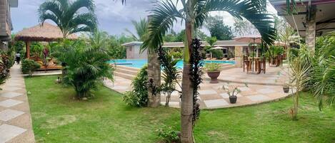 A tropical resort with a swimming pool, palm trees, and outdoor seating areas.