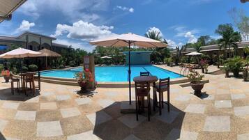 A pool area with lounge chairs and umbrellas, surrounded by potted plants and a stone-tiled patio.