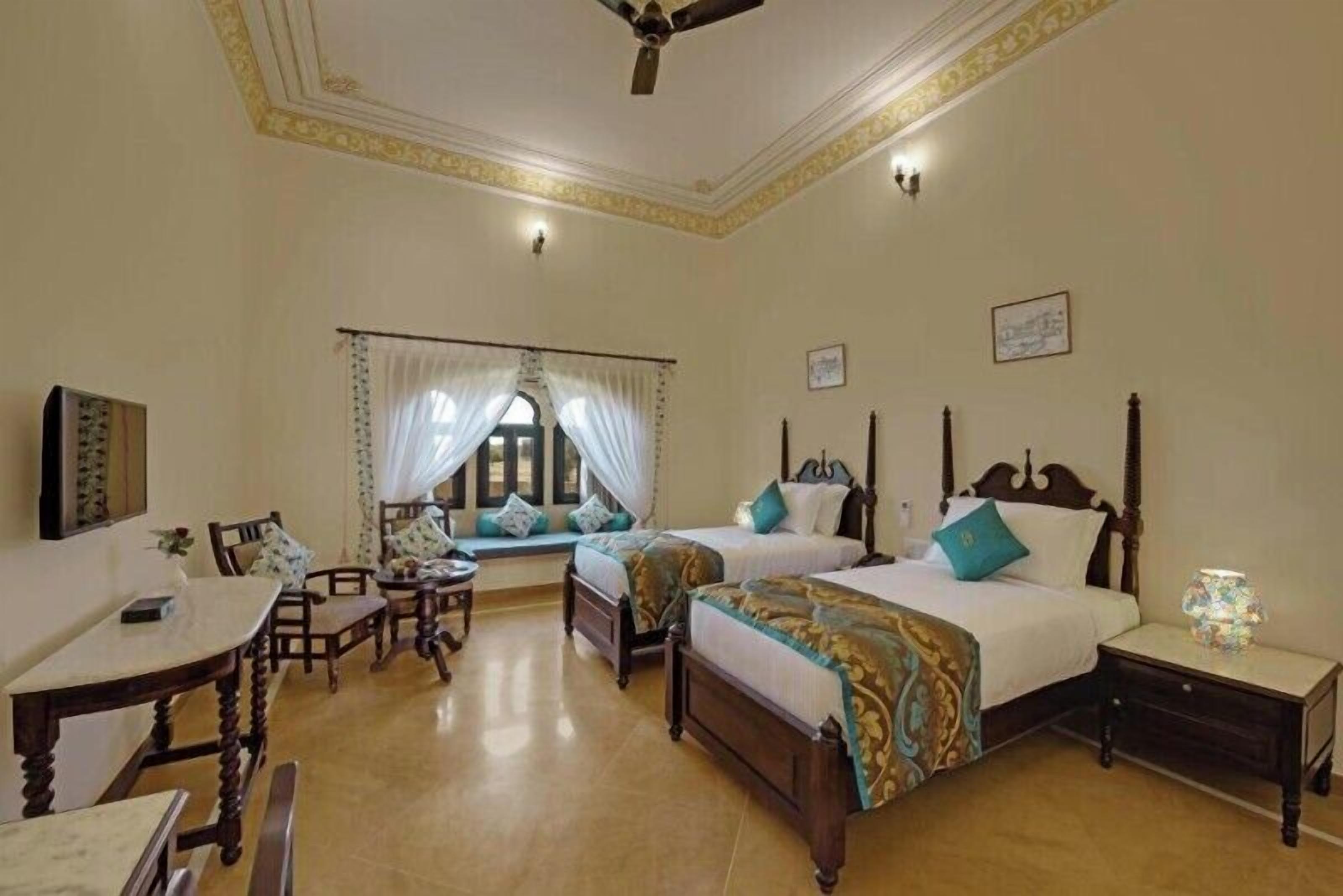 A hotel room with two beds, a dining area, and a window with curtains.