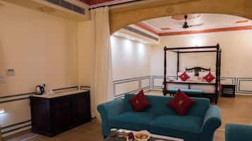 A hotel room with a four-poster bed, a teal sofa, a small table with a vase and snacks, and a dark wooden cabinet.