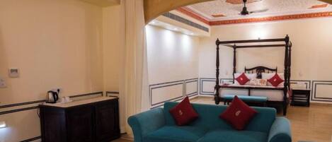 A hotel room with a four-poster bed, a teal sofa, a small table with a vase and snacks, and a dark wooden cabinet.