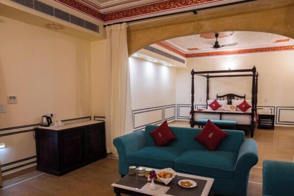 A hotel room with a four-poster bed, a teal sofa, a small table with a vase and snacks, and a dark wooden cabinet. - Skk The Fern, Jaisalmer (Jaisalmer)