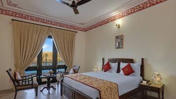 A hotel room with a large bed, a chair, a small table, and a ceiling fan.