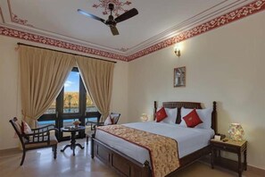 Una habitación de hotel con una cama grande, una silla, una mesita y un ventilador de techo.
