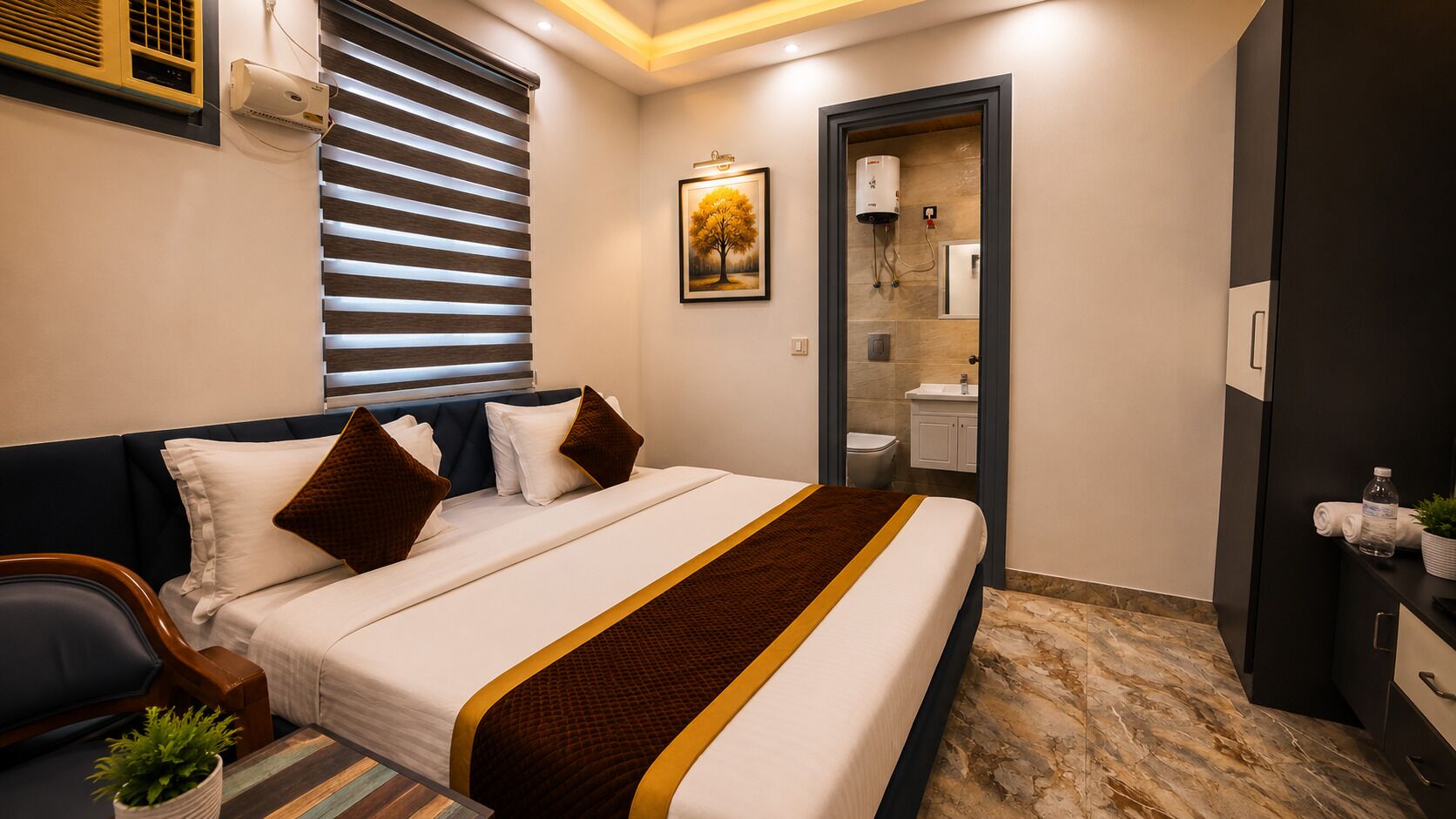 Ein Hotelzimmer mit Bett, Nachttisch mit Pflanze, Fenster mit Jalousien, einem durchgehenden Türspalt sichtbaren Badezimmer und einer wandmontierten Klimaanlage.