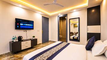 Una habitación de hotel moderna con cama, televisor, escritorio con cafetera y baño visible a través de una puerta abierta.