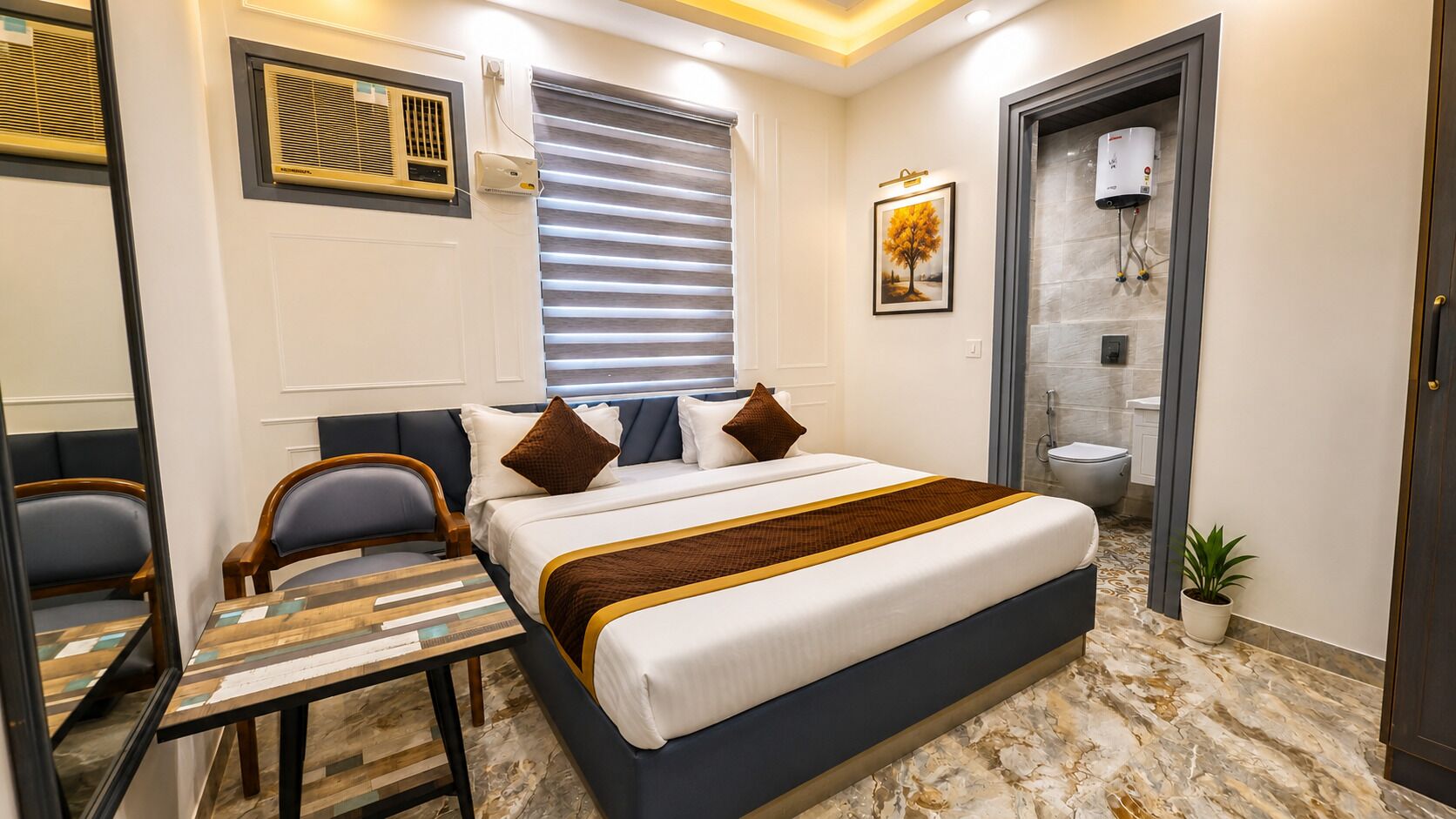 A hotel room with a bed, a desk, a chair, a window with blinds, a shower, and a potted plant.