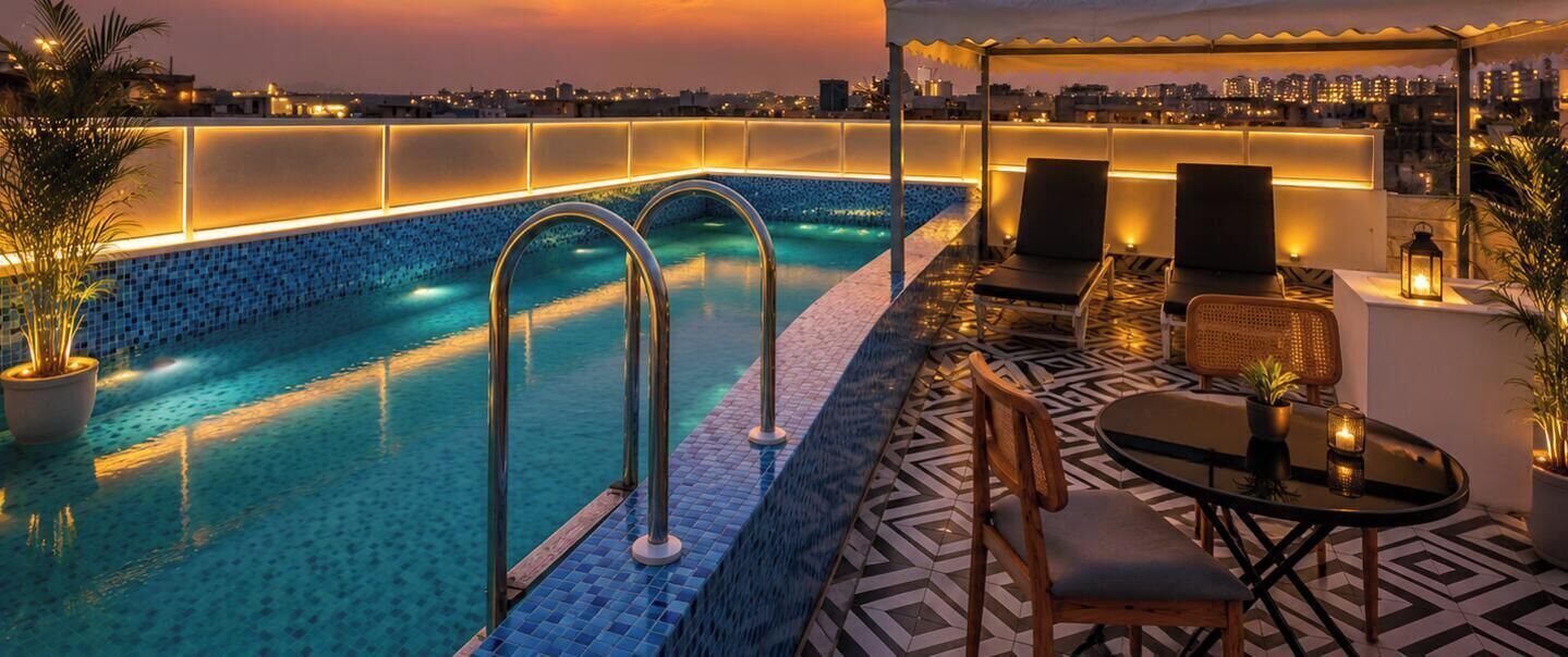 A rooftop pool with a city view, lounge chairs, and a table with a lantern.