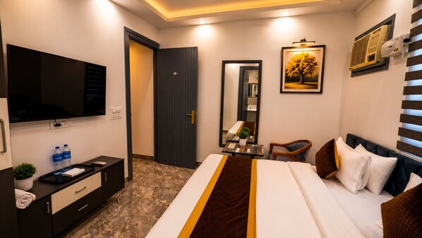Una habitación de hotel con cama, escritorio, silla, televisor y espejo.
