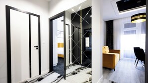 Una habitación de hotel moderna con piso de mármol, sofá amarillo y zona de comedor con una silla negra.