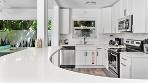 A modern kitchen with white cabinetry, stainless steel appliances, and a large window overlooking greenery. - ※ Villa Atlantico ※  3BR Beach house with a pool and a game-room (Fort Lauderdale)