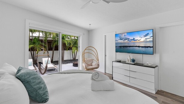 A modern bedroom with a large bed, a TV, a ceiling fan, and a view of a balcony with outdoor furniture. - ※ Villa Atlantico ※  3BR Beach house with a pool and a game-room (Fort Lauderdale)