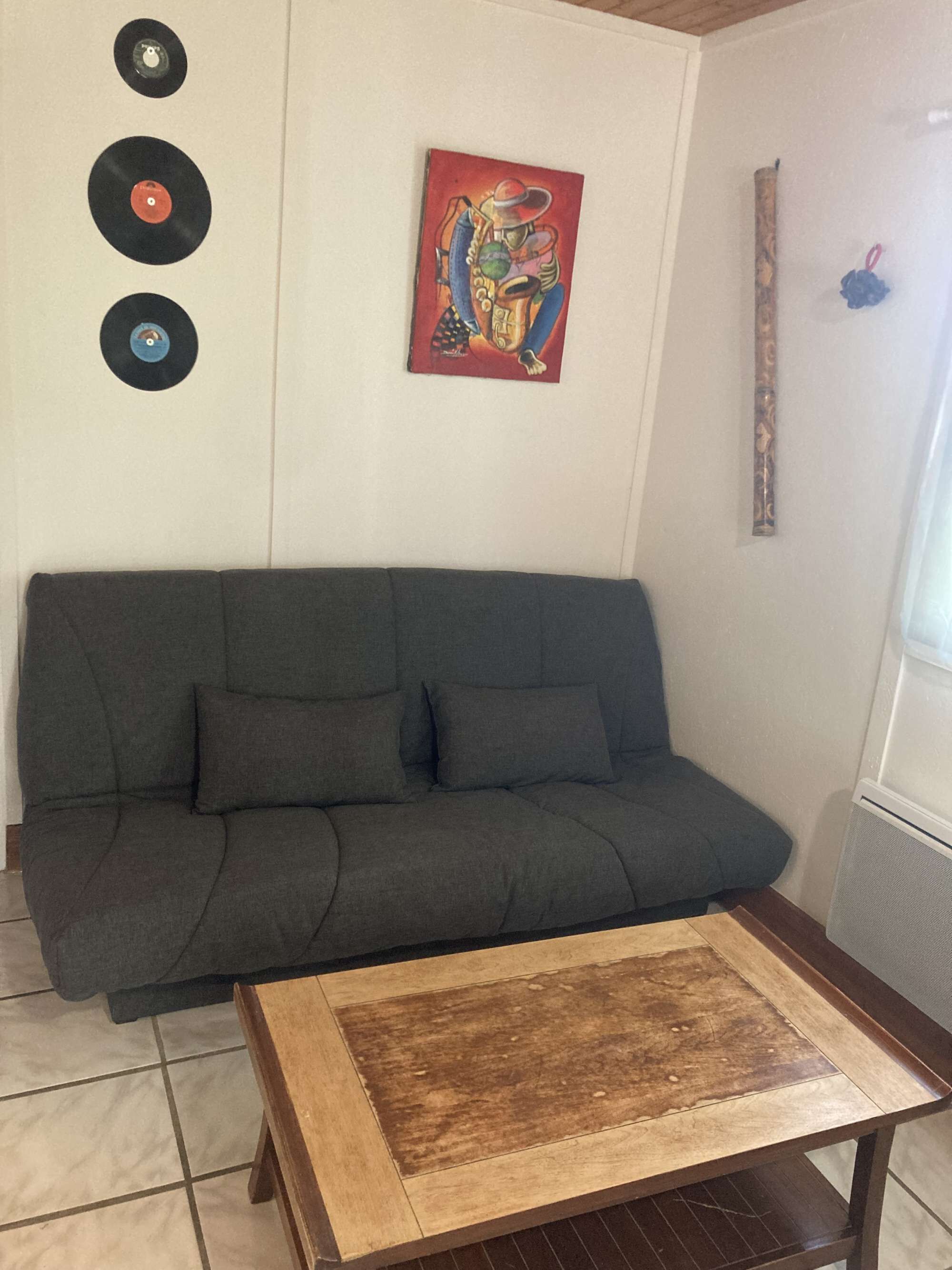 A living room with a dark green sofa, a wooden coffee table, and three vinyl records on the wall.