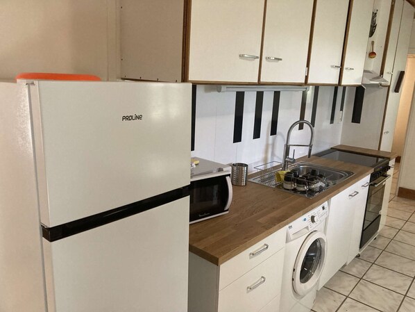 Une cuisine de taille réduite équipée d’un réfrigérateur, d’un évier, d’une cuisinière et d’un lave-linge.