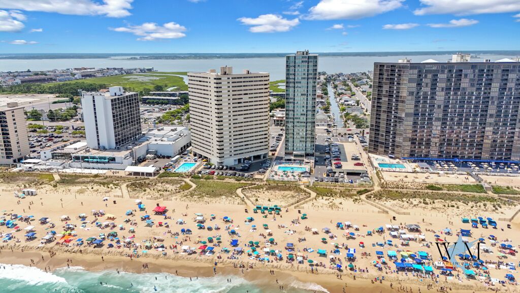 A coastal cityscape with a beach, high-rise buildings, and a marina.