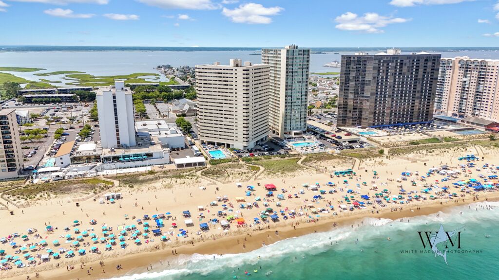 Vue aérienne d’une zone de plage avec un hôtel, une grande piscine et de nombreux parasols de plage.