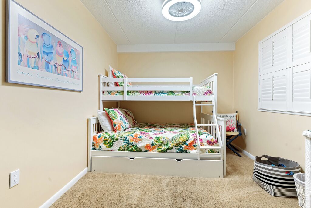 A bunk bed room with a floral bedspread, a ceiling fan, and a framed picture on the wall.