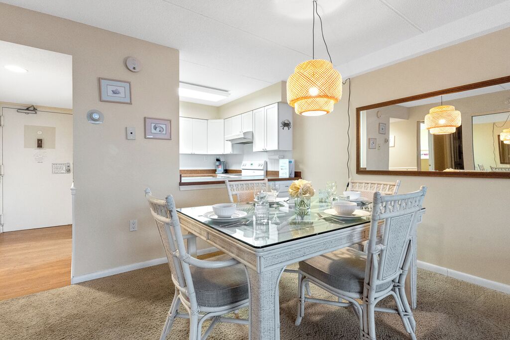 A dining area with a glass-top table, wicker chairs, and a hanging light fixture.