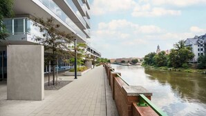 A riverside walkway adjacent to a modern building with a glass facade and a brick retaining wall. - Elegant Apartment close to Market Square | Balcony, WiFi (Wrocław)