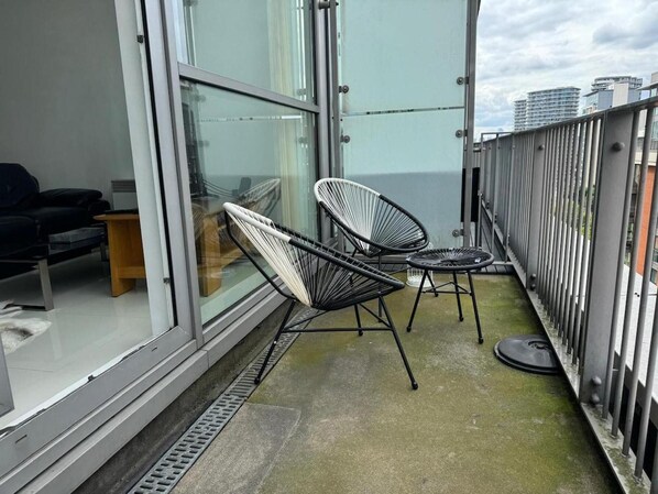 A balcony with two black wire-framed chairs, a small round table, and a sofa. - Royal Docks Luxury 3 Bedroom Apartment (London)