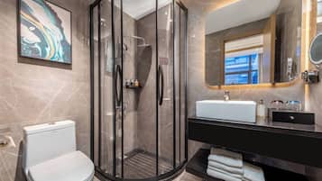Un baño moderno con ducha de vidrio, inodoro blanco, tocador negro con espejo y pared con azulejos de mármol.