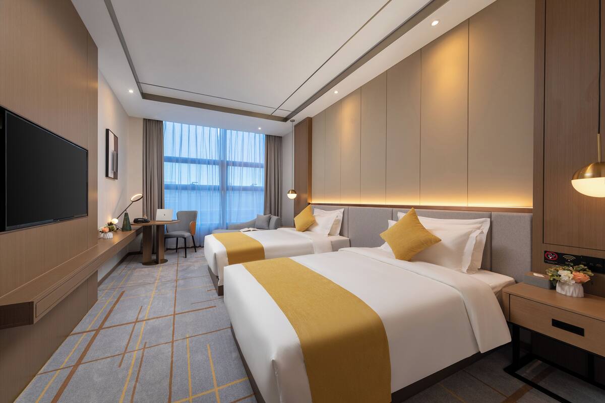 A hotel room with two beds, a desk, a TV, and a large window.