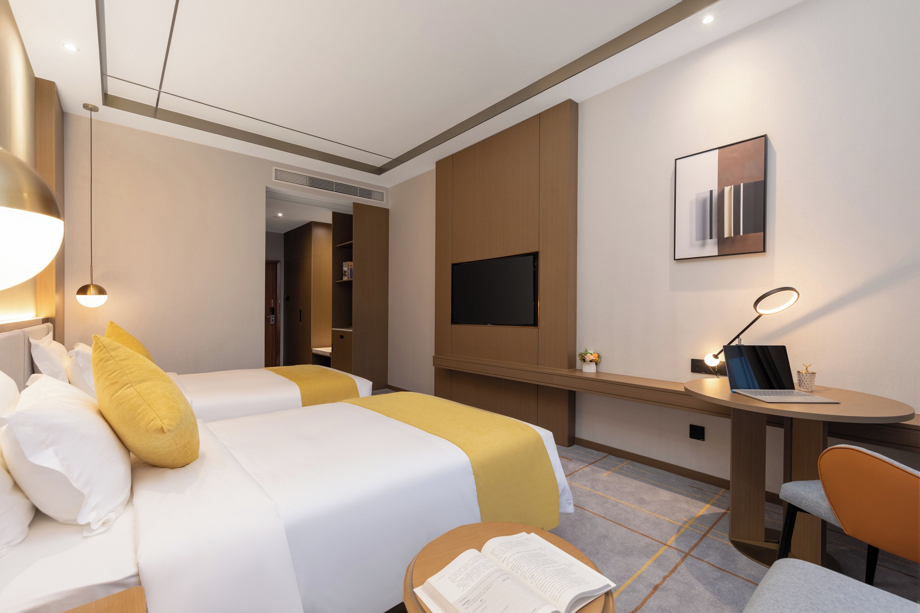 A hotel room with two beds, a desk, a chair, a TV, and a reading lamp.