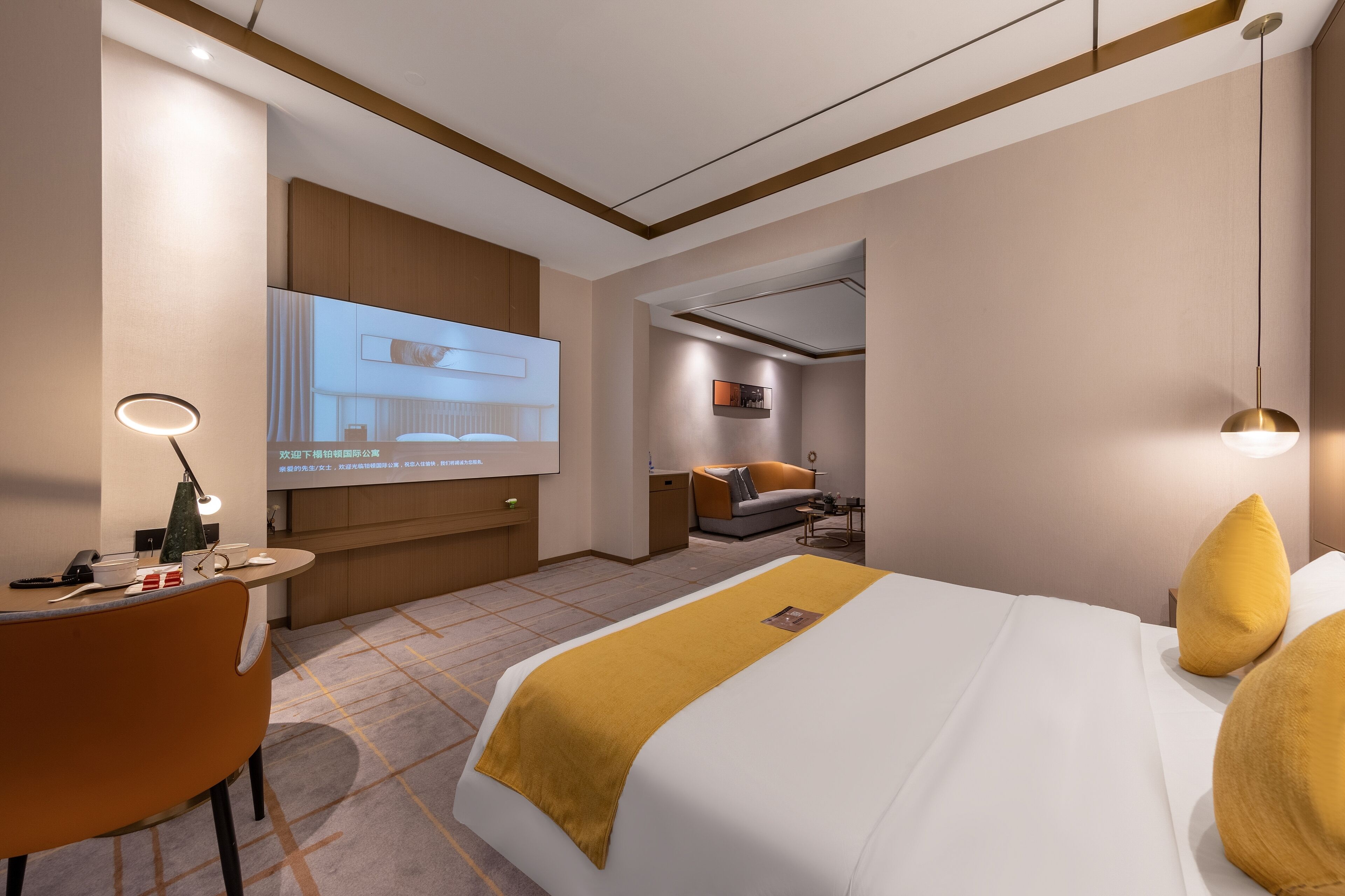 A hotel room with a bed, a desk, a chair, a TV screen, and a sofa.