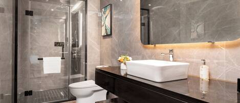 Un baño moderno con cabina de ducha de cristal, inodoro blanco, tocador negro con lavamanos blanco y un espejo grande.