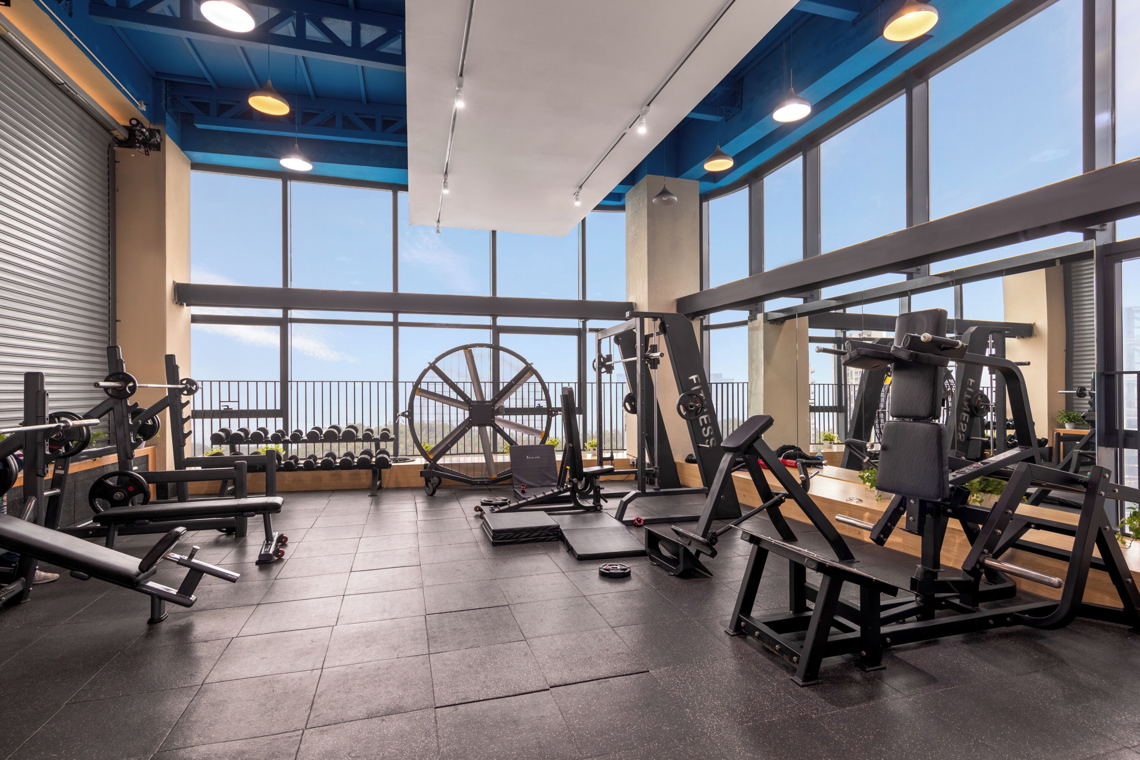 A gym with various exercise equipment, large windows, and a high ceiling.