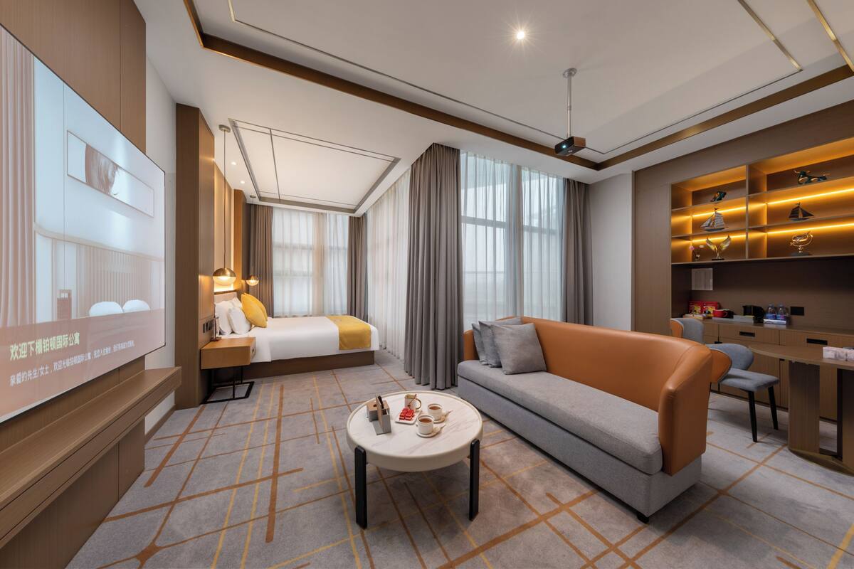 A modern hotel room with a bed, sofa, coffee table, and a desk area.