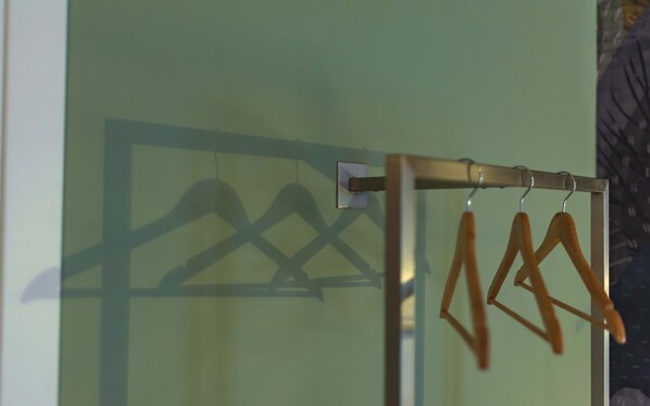 A metal rack with wooden hangers against a green wall. - Opera Boutique (Catania)