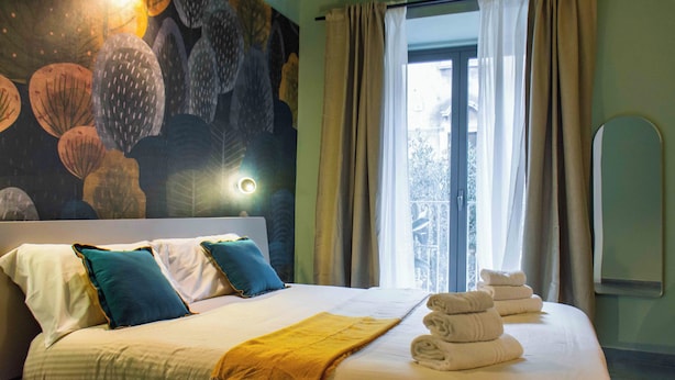 A hotel room with a bed, pillows, a blanket, and a window with curtains. - Opera Boutique (Catania)