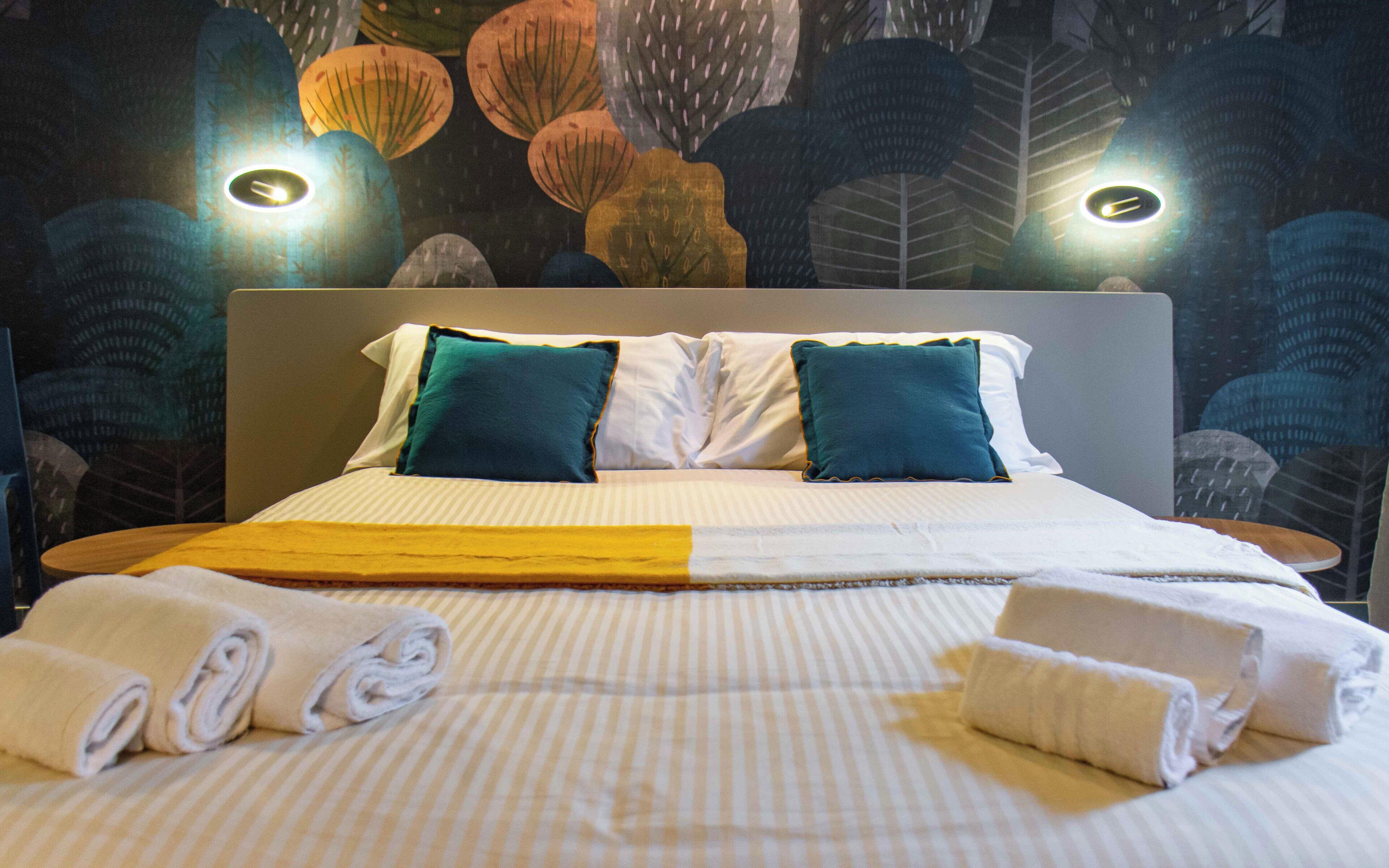 A neatly made bed with striped bedding, two pillows, and rolled towels.