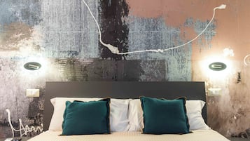 A bed with teal pillows, a white headboard, and a textured wall with two wall sconces.