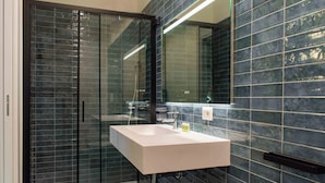 A modern bathroom with a glass shower enclosure, a white sink, and dark tiled walls. - Opera Boutique (Catania)