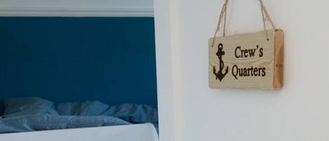 A bedroom with a bed, a wooden sign reading "Crew's Quarters," and a door with a brass handle.
