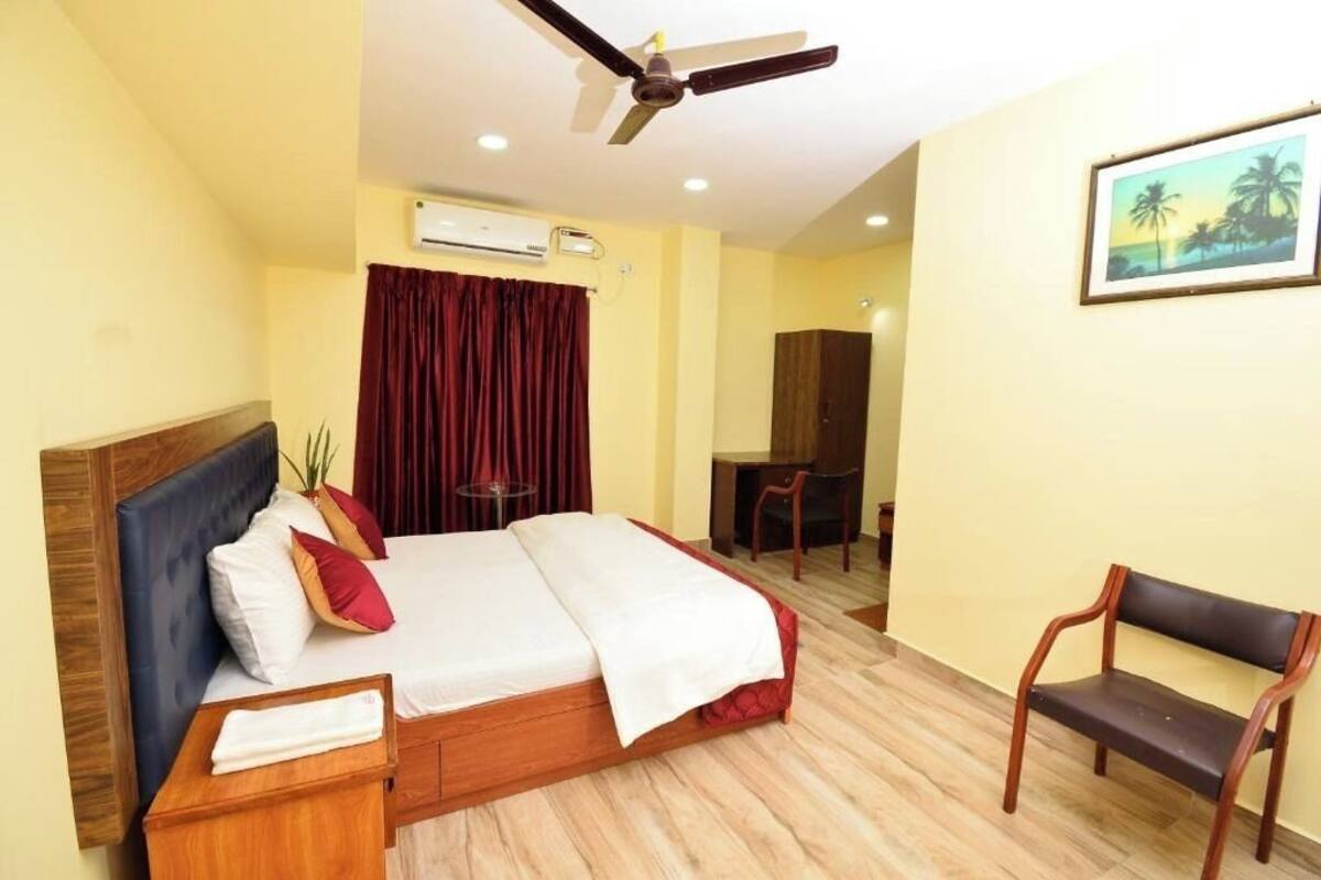 A hotel room with a bed, a desk, a chair, a ceiling fan, and an air conditioning unit.