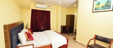 A hotel room with a bed, a desk, a chair, a ceiling fan, and an air conditioning unit.