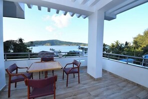 A covered outdoor seating area with a table and chairs, overlooking a body of water and hills.