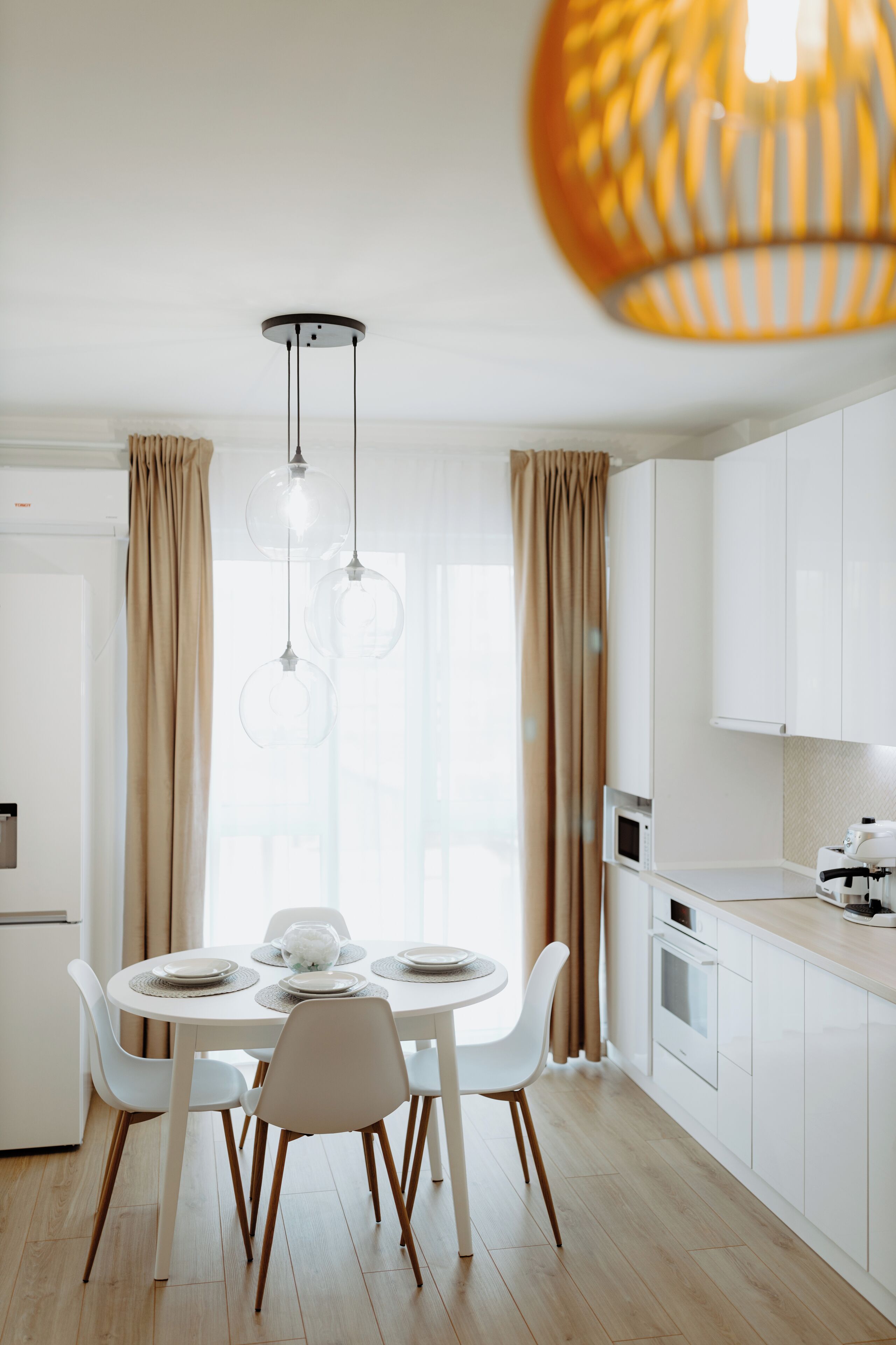 Une cuisine moderne avec des meubles blancs, une table de salle à manger ronde entourée de chaises et des luminaires suspendus.