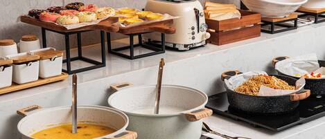 A buffet setup with various food items, including pastries and a pot of soup, on a kitchen counter.