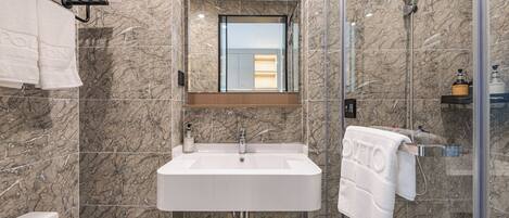 A modern bathroom with a marble backsplash, a white sink, and a glass shower enclosure.