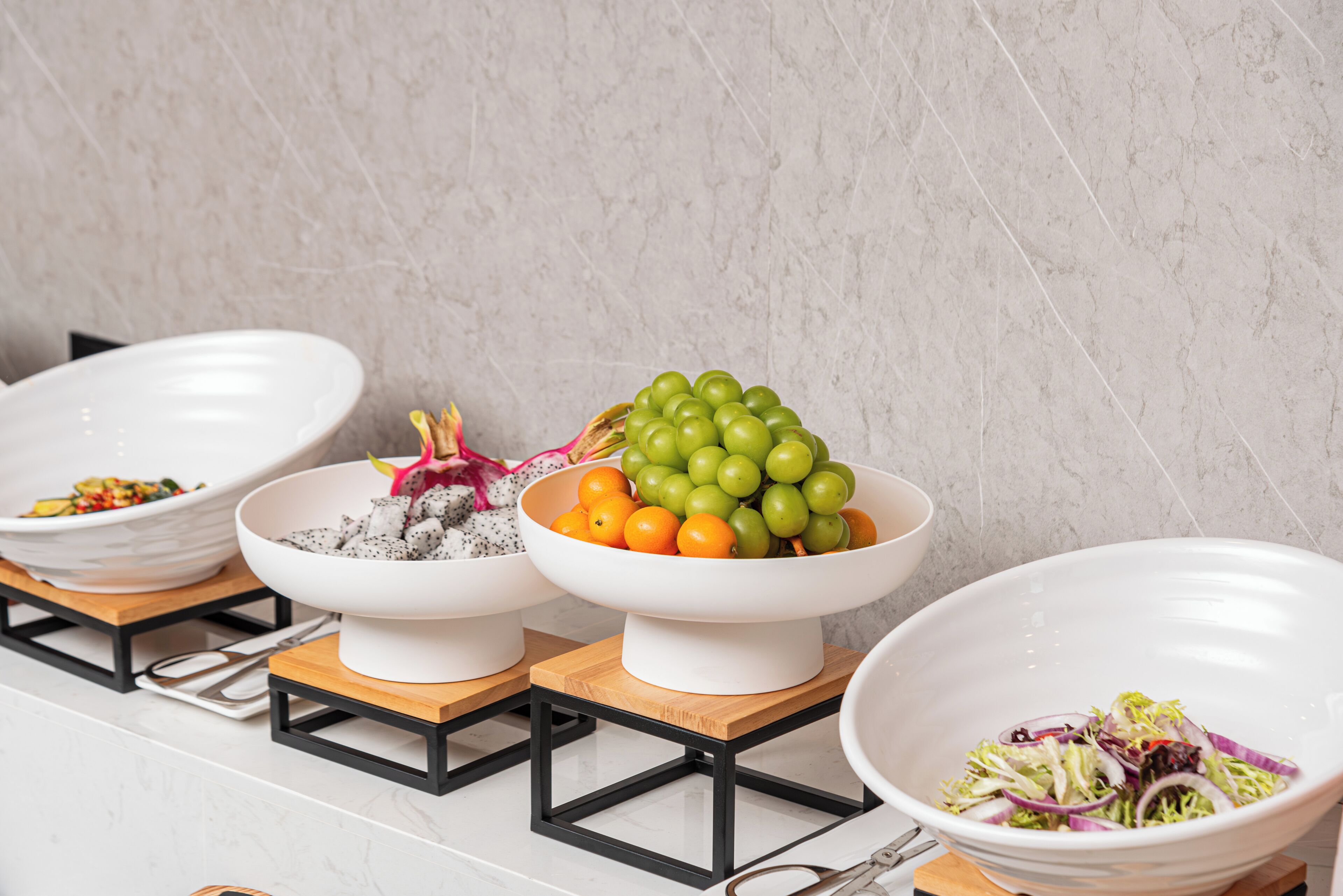 A kitchen counter with three white bowls on wooden stands, each containing different food items.