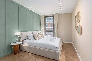 A modern bedroom with a large bed, a small round table, and a window with curtains.