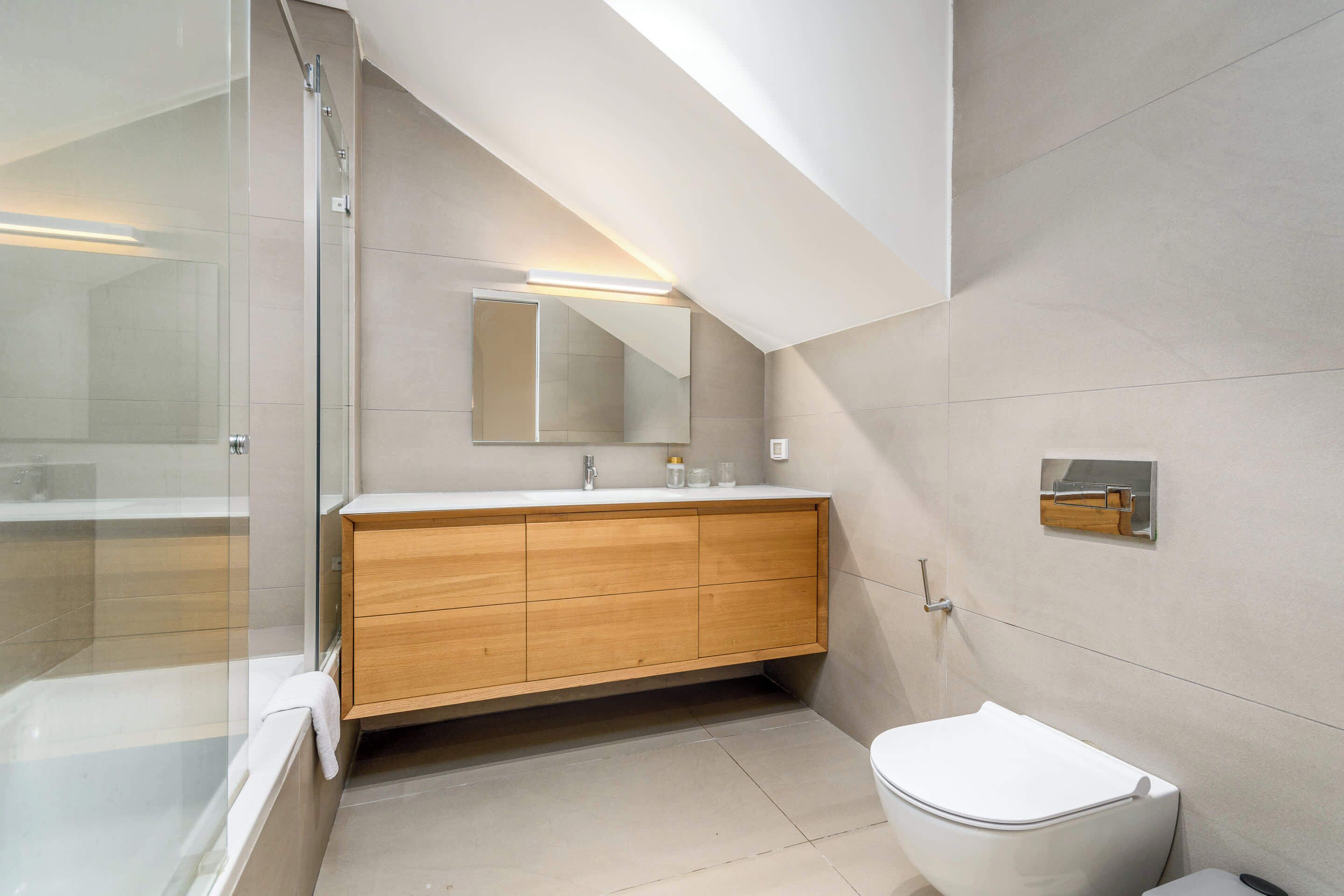 A modern bathroom with a glass shower enclosure, a wooden vanity, and a white toilet.