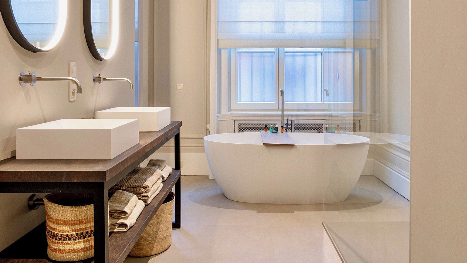 Une salle de bain moderne avec deux lavabos, une grande baignoire et une fenêtre équipée de stores.