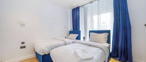A double room with two beds, a large window with blue curtains, and a wooden floor.