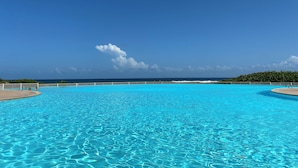 Une grande piscine d’un bleu éclatant, avec vue sur l’océan, et une clôture blanche qui l’entoure.