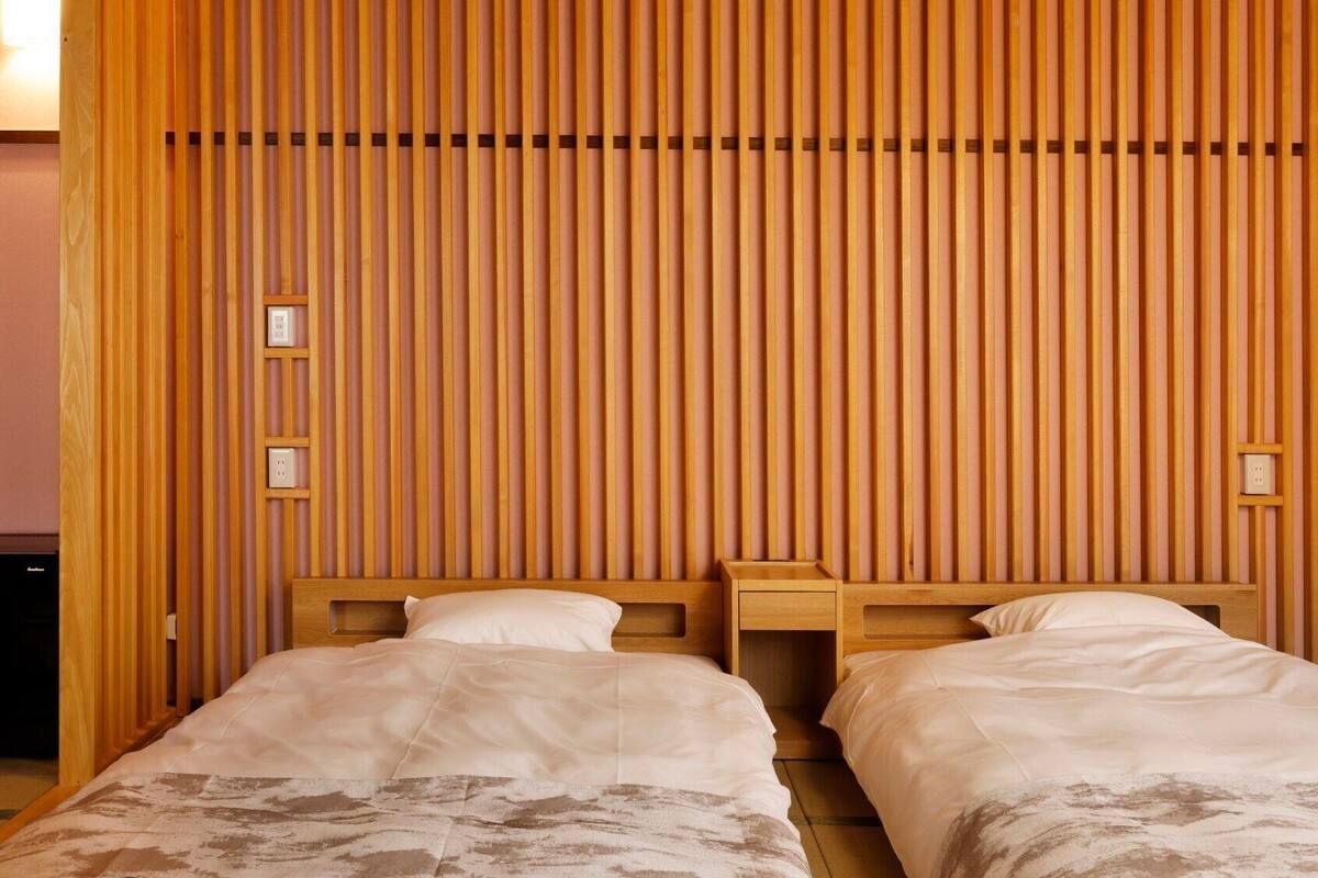 A hotel room with two beds, a wooden slatted wall, and a small bedside table with a lamp.